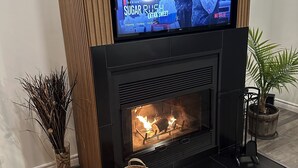 Una sala de estar moderna con un televisor de pantalla plana sobre una chimenea, una planta en maceta y una cesta decorativa en el suelo.