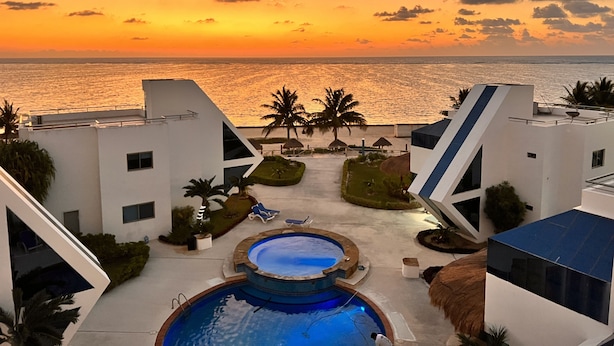 Un complexe hôtelier doté d’une piscine, de palmiers et offrant une vue imprenable sur le coucher de soleil.