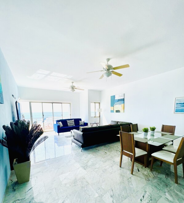 A spacious living area with a dining table, chairs, a sofa, and ceiling fans.