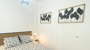 Een slaapkamer met een bed, een nachtkastje, een lamp en twee kunstwerken aan de muur.