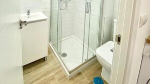 Een moderne badkamer met een douchecabine van glas, een witte wastafel en een toilet.