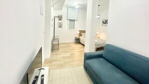 Een knus woongedeelte met een bank, een kleine tafel, een vloerlamp en een bed met beddengoed met een patroon.