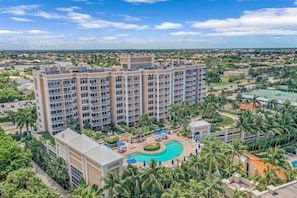 Ein mehrstöckiges Hotel mit einem zentralen Pool, umgeben von Palmen und Liegebereichen.