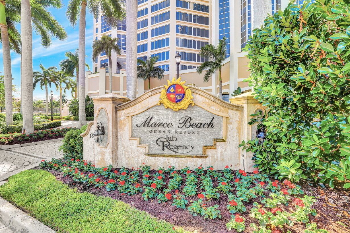 A sign for Marco Beach Ocean Resort Club Regency with a landscaped garden in front.