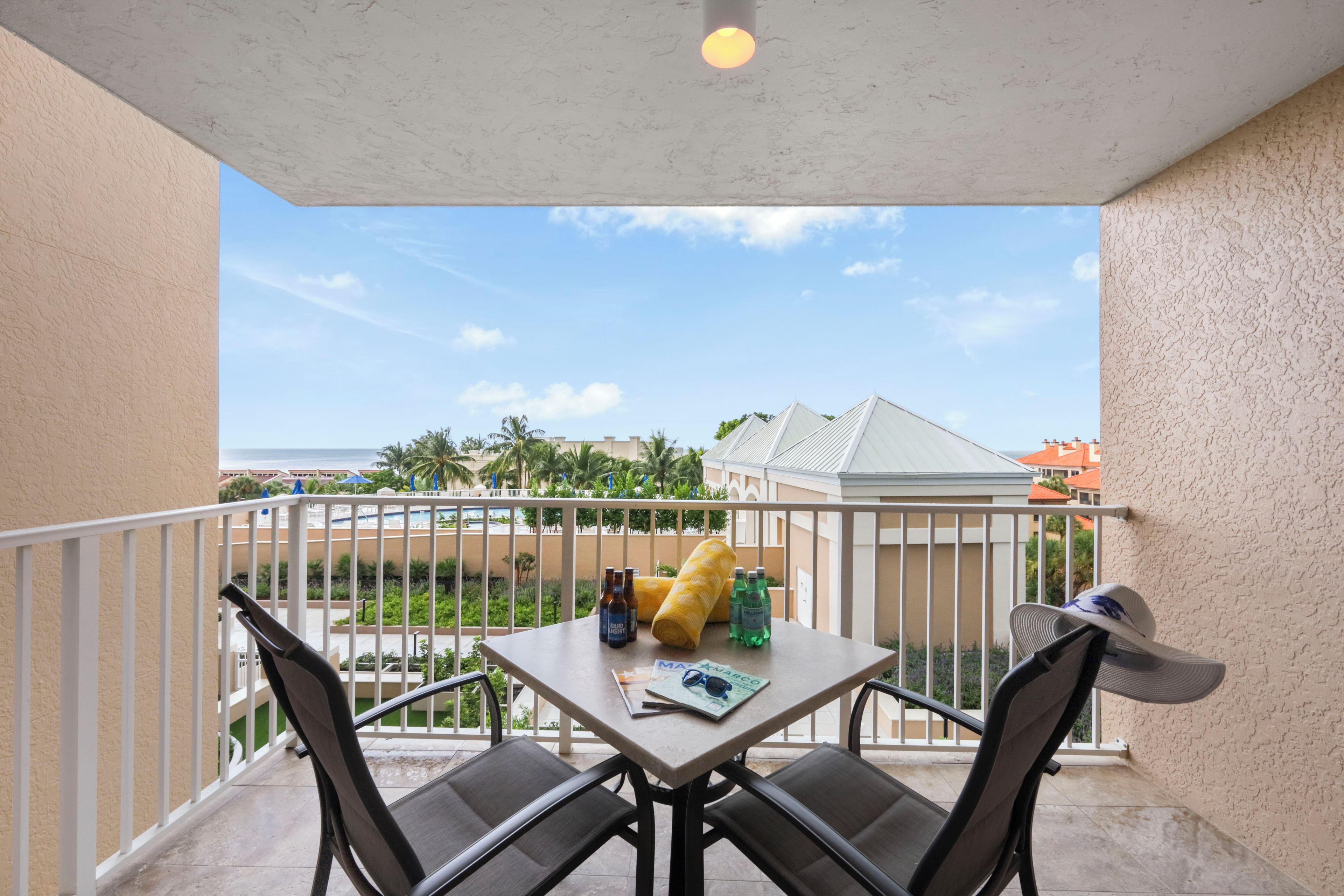 A balcony with a table, chairs, and a view of a pool and buildings.