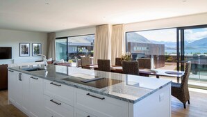 A modern kitchen with a large island, white cabinetry, and a view of mountains and water. - Waimaori Views The Sp (Wānaka)