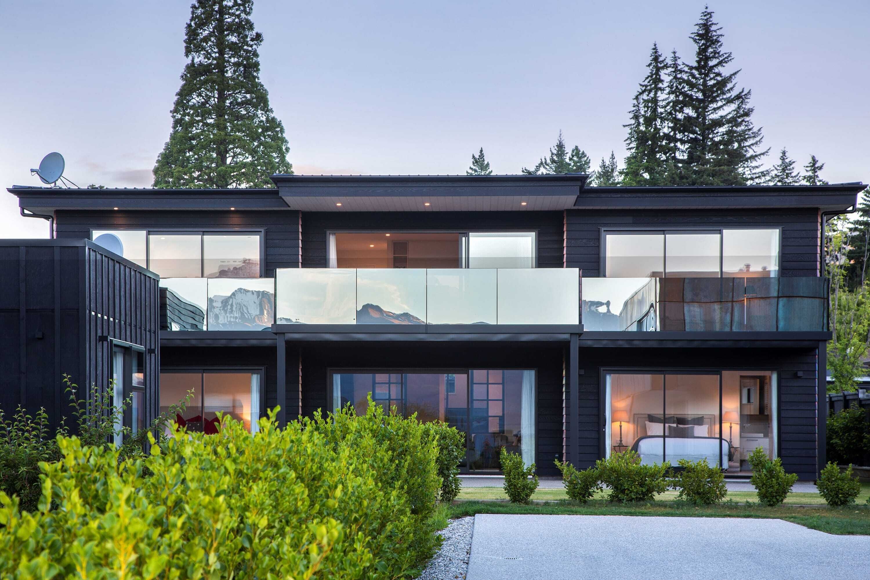 Une maison moderne à deux étages, dotée de grandes fenêtres en verre, d’un balcon et d’une antenne parabolique.