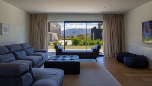 A modern living room with a large window, a sofa, an ottoman, and a bean bag. - Waimaori Views The Sp (Wānaka)