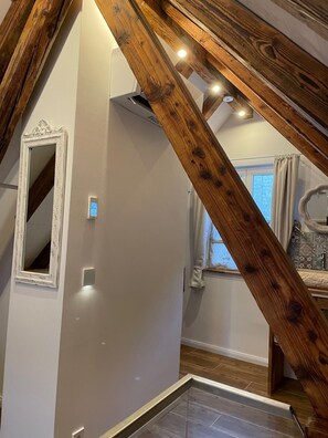 Cozy loft space with a sloped ceiling, featuring a window with white curtains and a wooden beam structure.