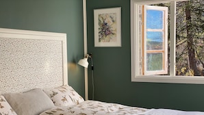 A bedroom with a bed, a window, a wall-mounted lamp, and a framed picture.