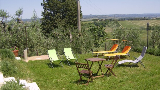 An outdoor seating area with lawn chairs and a table, surrounded by greenery and a view of a vineyard. - Old Tuscan farmhouse in the heart of Tuscany powered by green energy (Gambassi Terme)