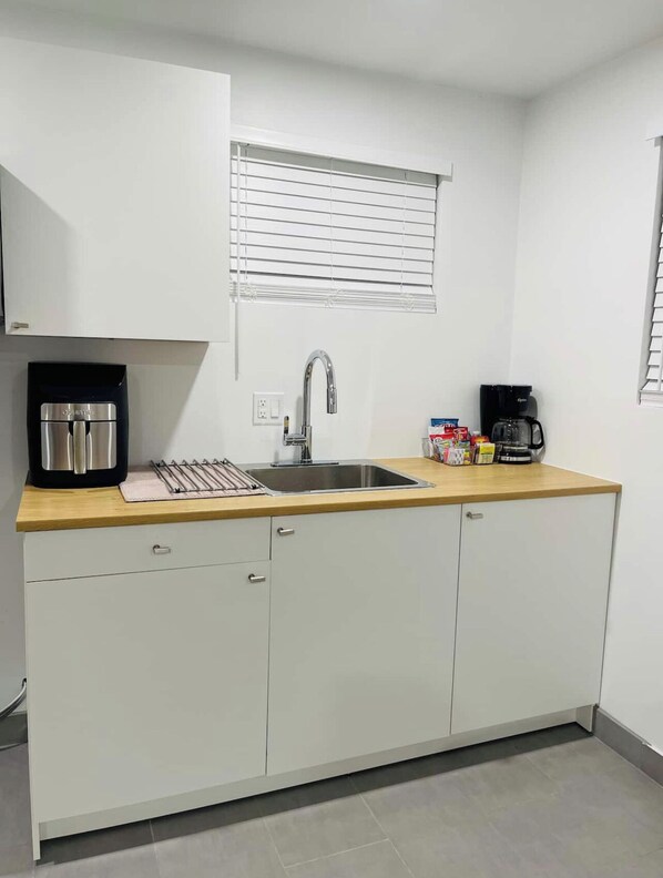 A compact kitchen with a sink, a coffee maker, and a kettle on the countertop.