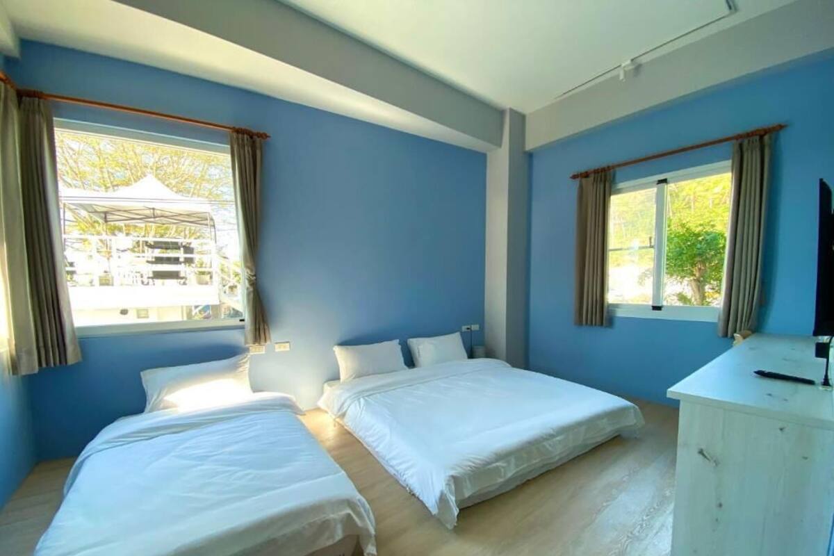 A room with two beds, a wooden floor, a white cabinet, and a window with curtains.