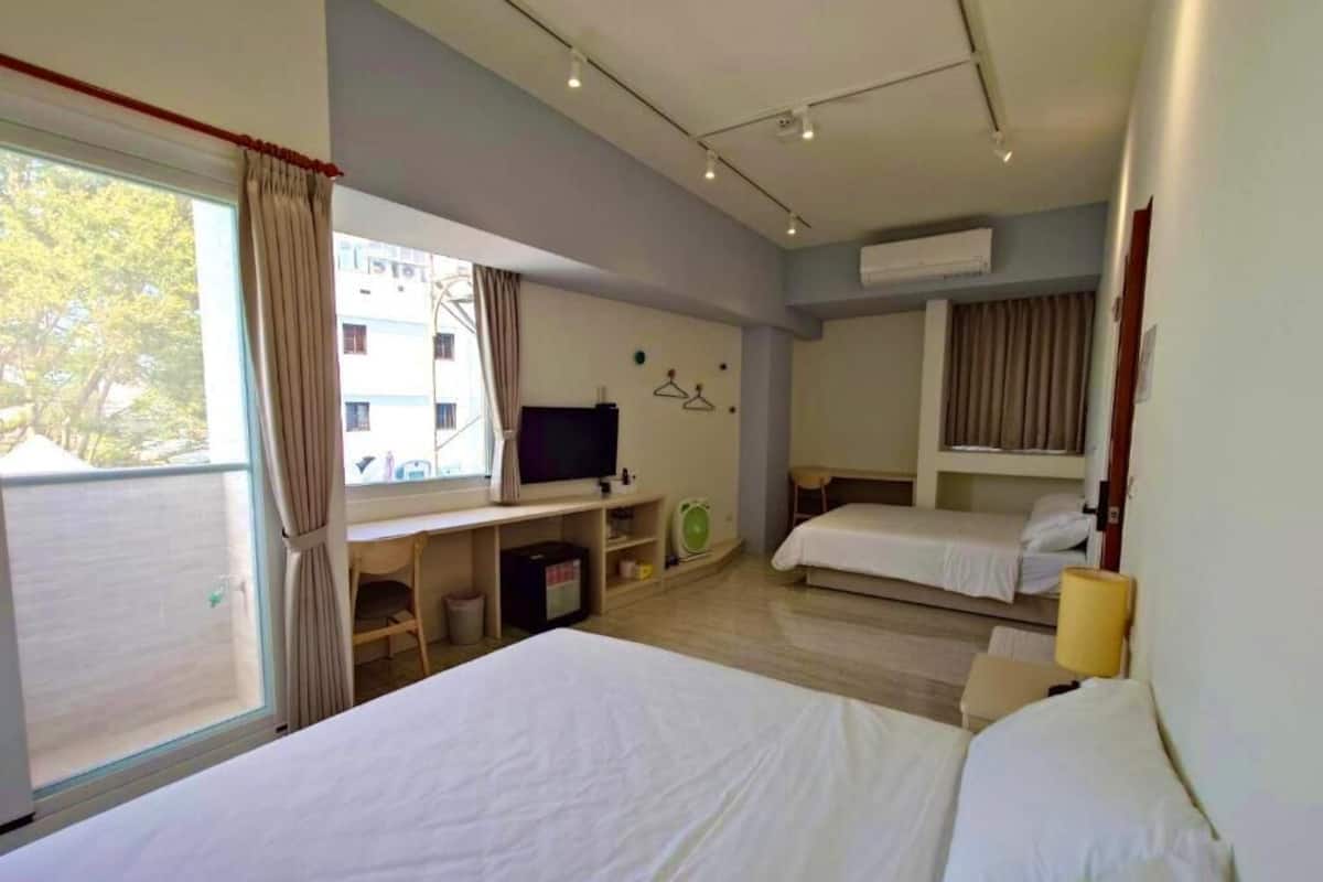 A hotel room with a large bed, a desk with a computer, a TV, and a window with curtains.