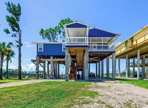 Une maison à deux étages dotée d’un balcon au niveau supérieur, soutenu par des piliers en béton, et d’une zone couverte au rez-de-chaussée.