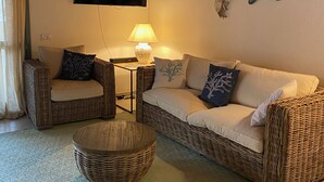 Ein gemütliches Wohnzimmer mit Korbmöbeln, einem Flachbildfernseher, dekorativer Wandkunst mit Sternenmotiven und einem gemusterten Teppich.