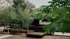 A wooden deck with a table and chairs, surrounded by trees and a building with a covered area.
