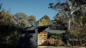 A modern building with a dark facade, a wooden door, and a small overhang.