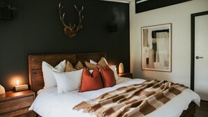 A bed with a wooden headboard, white and brown pillows, a brown blanket, and a mounted antler on the wall. - The Artemis Cottage - Romantic Couples Retreat (Woodlands)