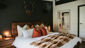 Un lit avec une tête de lit en bois, des oreillers blancs et bruns, une couverture marron et une paire de bois de cerf accrochée au mur.