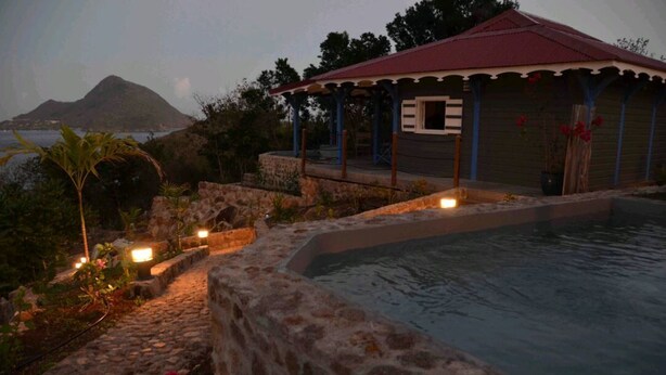 Zona de piscina con pared de piedra y un pequeño edificio de techo rojo.