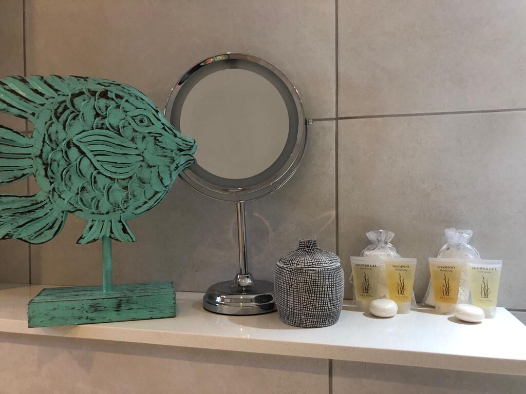 A bathroom vanity with a mirror, a decorative fish sculpture, a patterned vase, and toiletries.