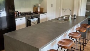 A modern kitchen with a central island, bar stools, pendant lights, and stainless steel appliances.