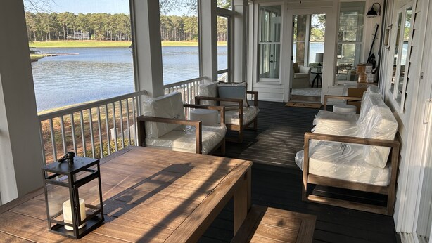 En inglasad veranda med trämöbler, stora fönster och utsikt över en sjö.
