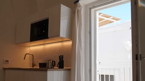 Una cocina compacta con microondas, lavamanos y una pequeña encimera. Una puerta corrediza de vidrio da a un balcón.
