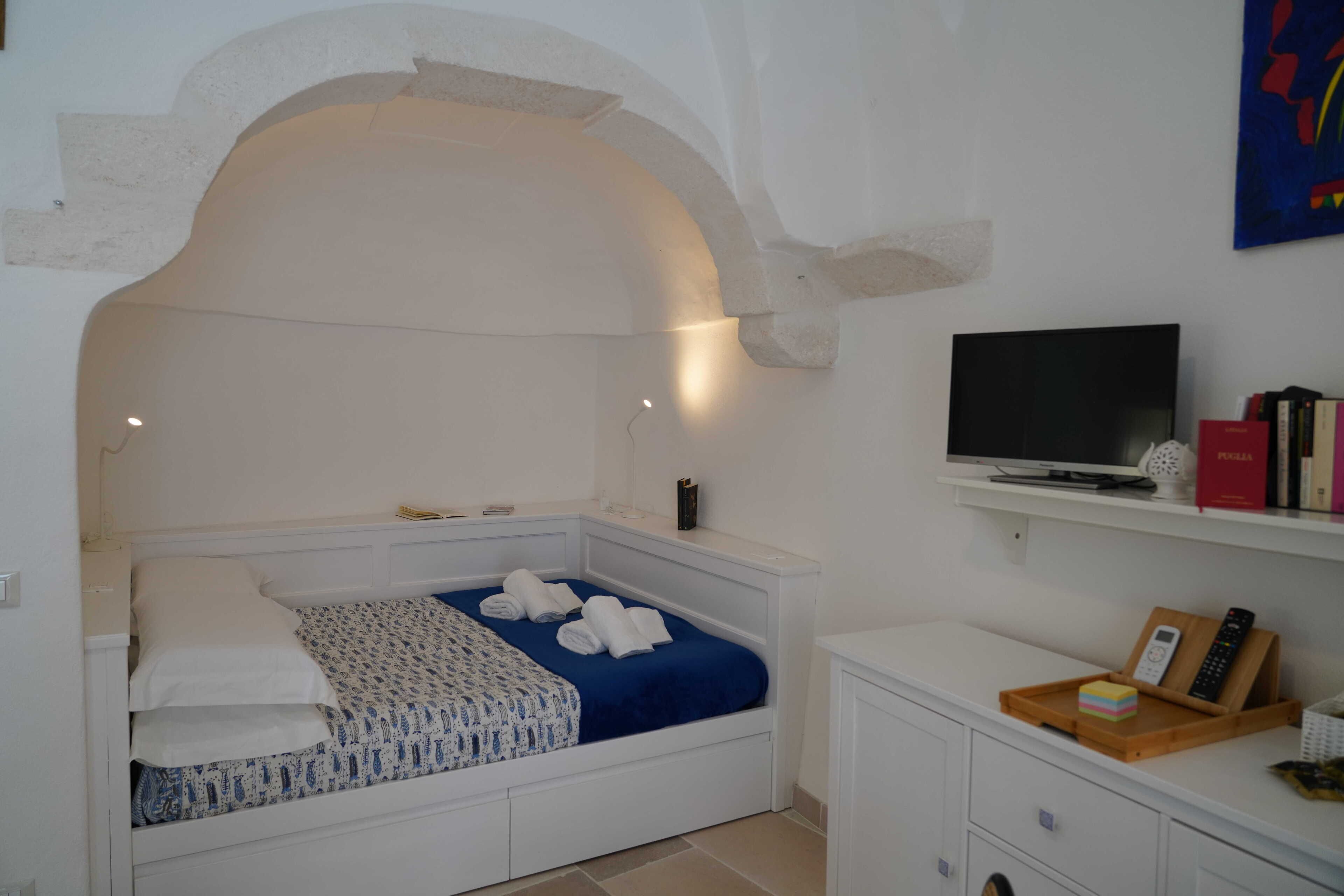 A bedroom with a bed, a television, and a shelf with books and a remote control.