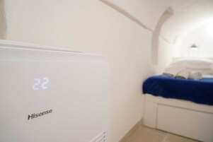 Una habitación con un aire acondicionado Hisense blanco, una cama con cubrecama azul y un cabecero blanco.