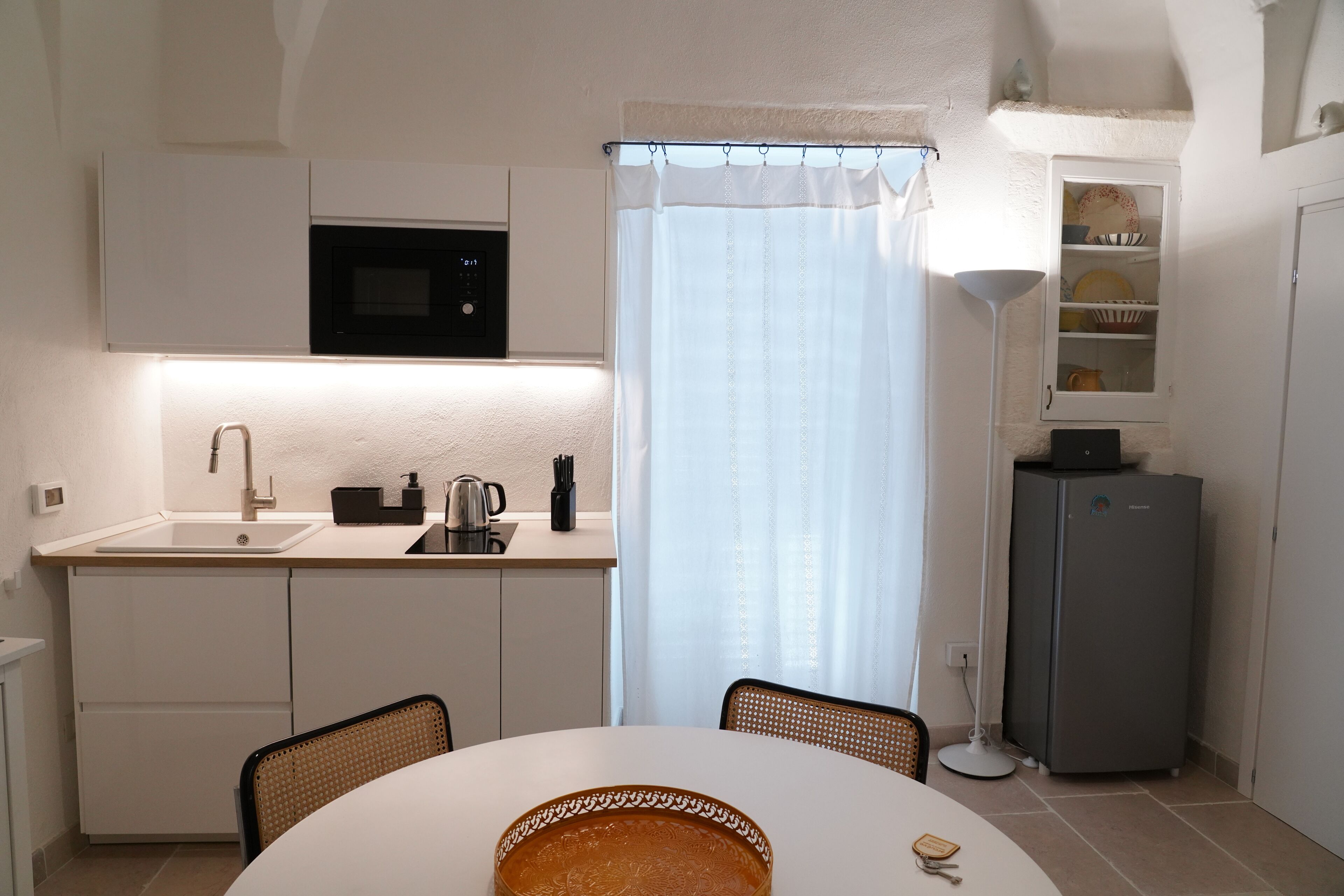 A compact kitchen with a microwave, sink, and cabinets. There's a dining table with chairs and a basket.