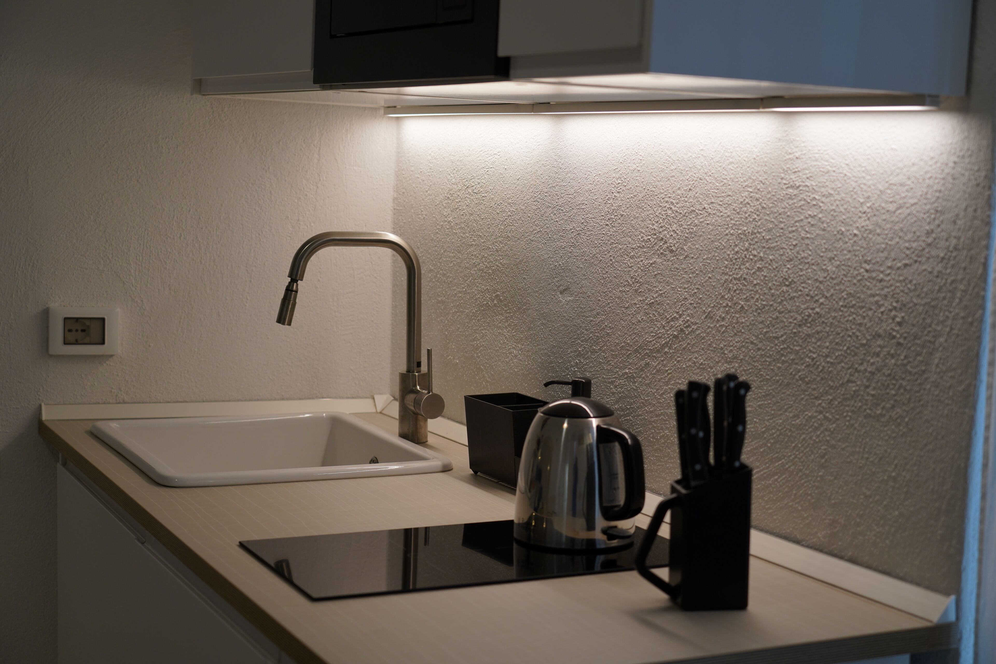 Eine moderne Küche mit einem weißen Spülbecken, einem Edelstahl-Wasserhahn und einem Wasserkocher auf der Arbeitsplatte.