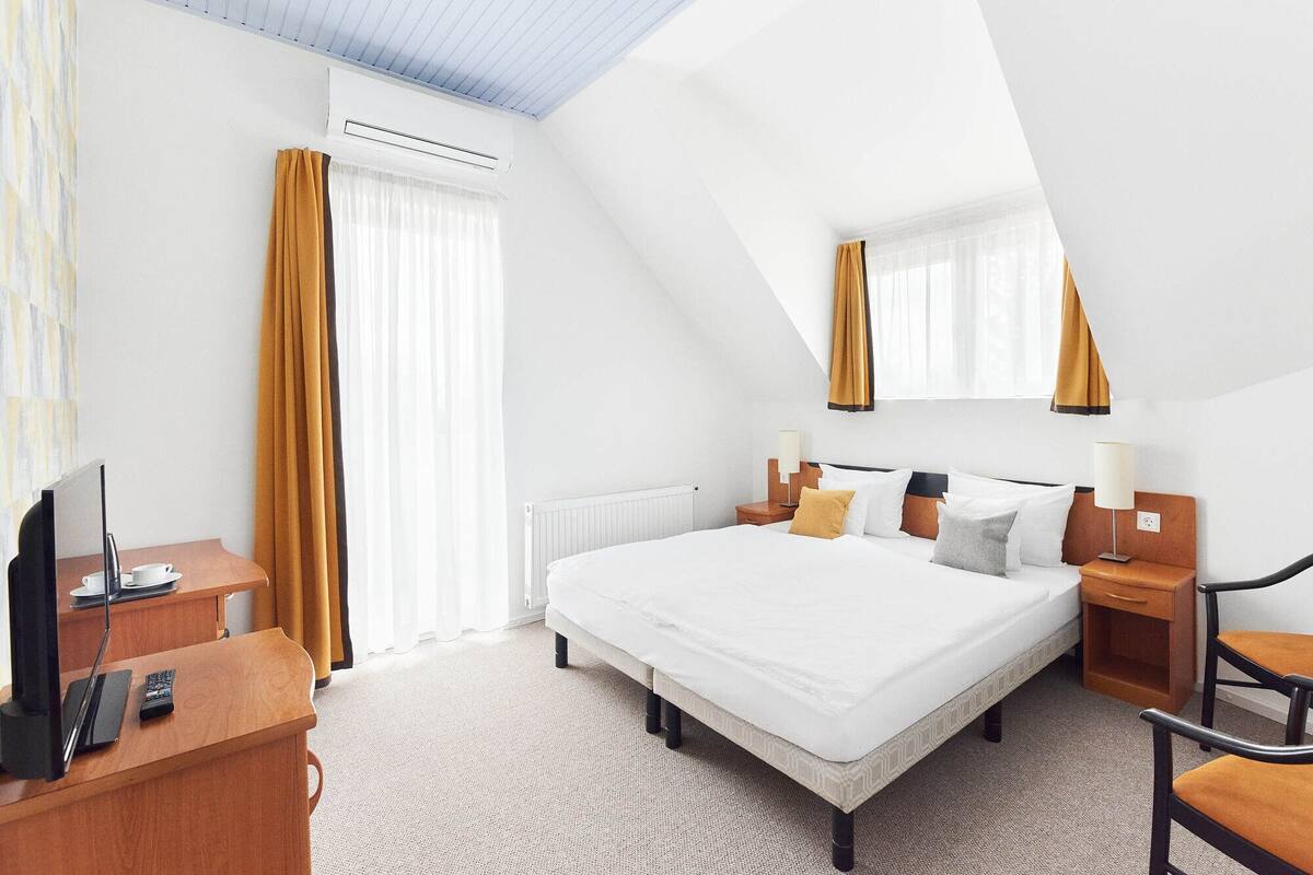 A hotel room with a large bed, a desk with a television, and a window with curtains.