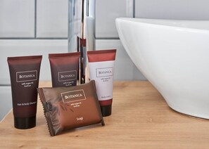 Three Botanica hair and body care products, including a shampoo, body lotion, and soap, displayed on a wooden surface in a bathroom. - Lorelei Pension Adults Only (Gyenesdias)