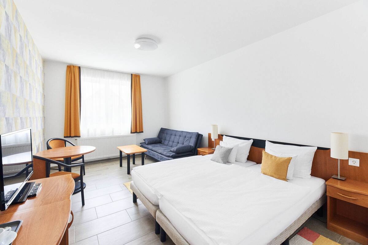 A hotel room with a large bed, a desk with a chair, a sofa, and a TV.
