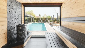 A modern indoor pool area with a stone wall, wooden benches, and a clear view of the outside. - Lorelei Pension Adults Only (Gyenesdias)