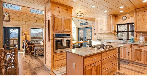 Interno di una baita in legno con cucina, sala da pranzo e un'ampia finestra su un paesaggio montano.
