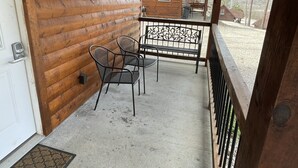 A wooden cabin with a covered porch, a metal table and chairs, and a view of a small building in the background. - Cozy Cabin on the edge of town only 1/2 mile from Current River ! (Van Buren)