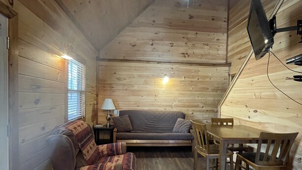 A cozy cabin interior with a wooden floor, a sofa, a dining table with chairs, and a lamp. - Cozy Cabin on the edge of town only 1/2 mile from Current River ! (Van Buren)