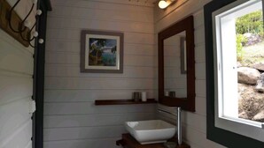 A bathroom with a white sink, a framed painting, and a window with a view of rocks and greenery. - Cases créoles classified 4**** with private pools (Terre-de-Bas)
