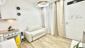 A compact living space with a kitchenette, a white sofa, a dining table with yellow chairs, and a large window with curtains. - Mejorana Apartament (1 bedroom apartment) (Madrid)