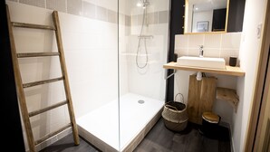 A modern bathroom with a glass shower enclosure, a wooden ladder, a sink with a wooden vanity, and a mirror.