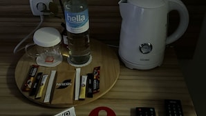 Une table en bois avec une bouteille d’eau, une machine à café, un sachet de thé et divers en-cas. On y trouve également deux télécommandes et une pancarte indiquant : « Veuillez ne pas déranger ».