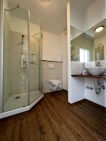 Un baño moderno con ducha de vidrio, inodoro y lavamanos con espejo.
