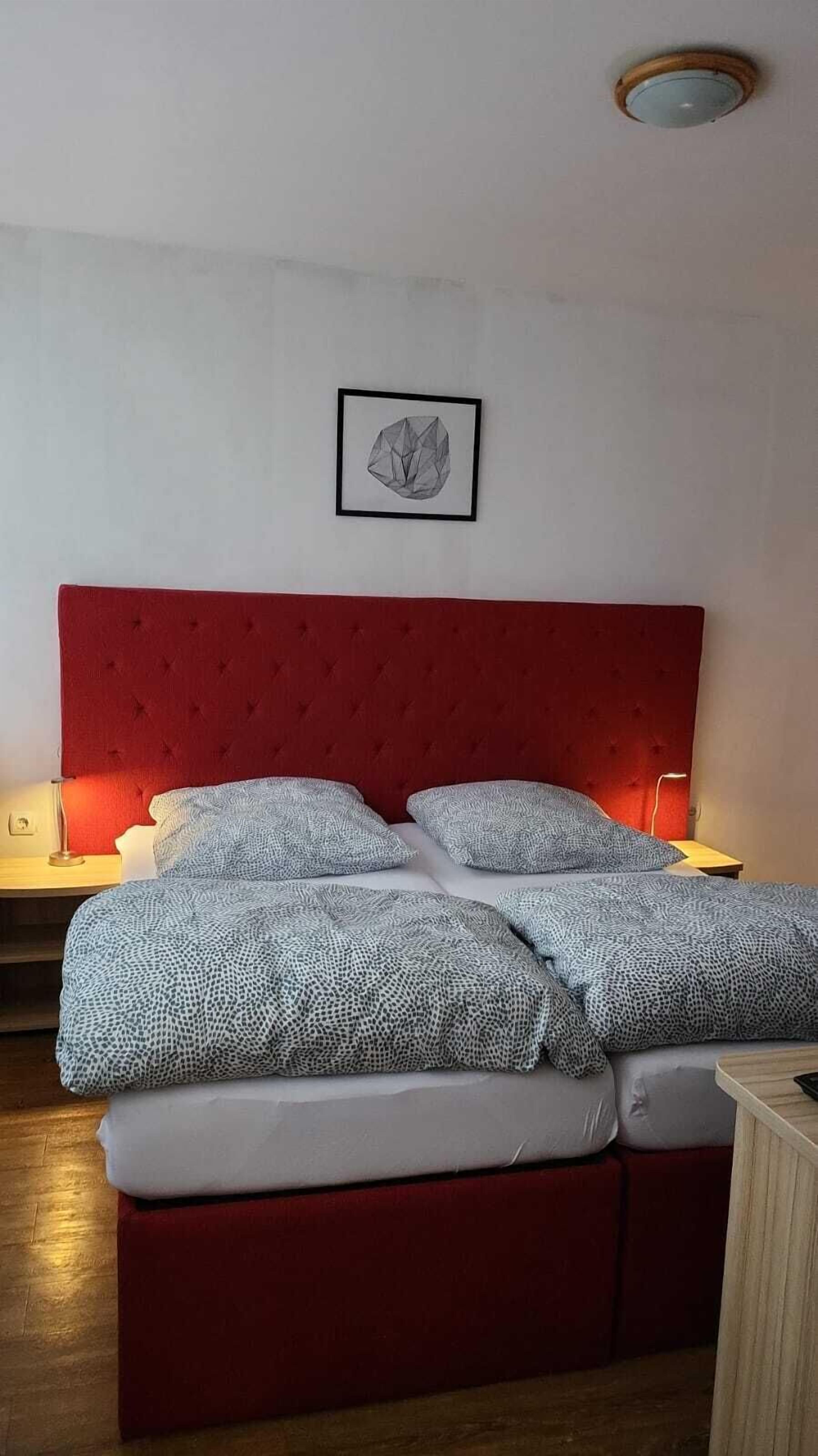 A bed with a red headboard, two bedside tables with lamps, and a framed picture on the wall.