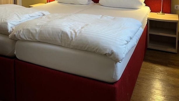 Un lit double avec une tête de lit rouge, deux tables de chevet avec des lampes et un plancher en bois.