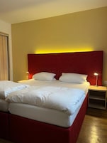 Una cama doble con cabecera roja, dos mesitas de noche con lámparas y suelo de madera.