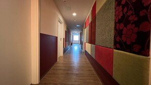 Un long couloir étroit aux murs peints alternativement en rouge et en gris, doté d’un plancher en bois et d’un plafond pourvu d’un éclairage encastré.