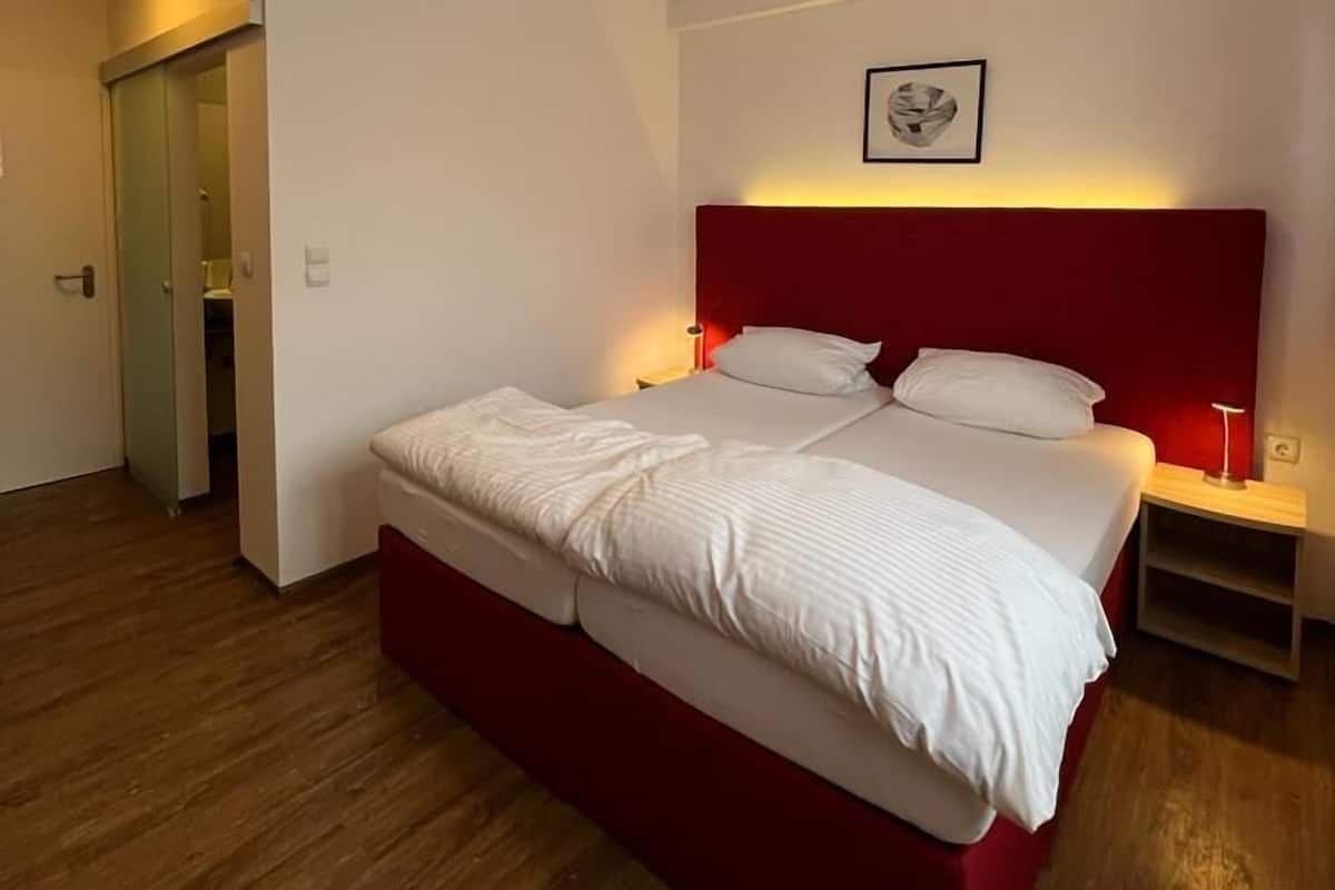 Une chambre moderne avec un grand lit, un plancher en bois et une tête de lit rouge.